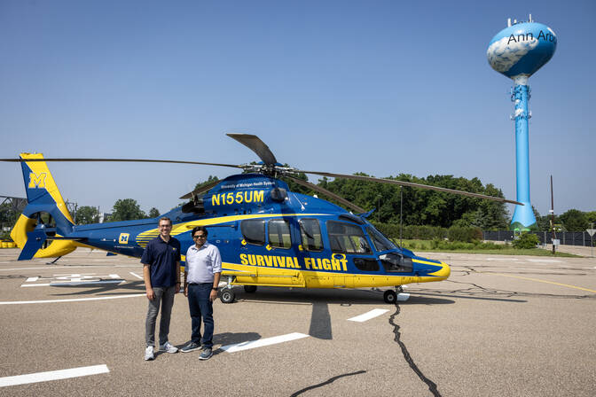McGuire and Viswanathan stand in front of the helicopter, painted in blue and yellow with "SURVIVAL FLIGHT" on the side.