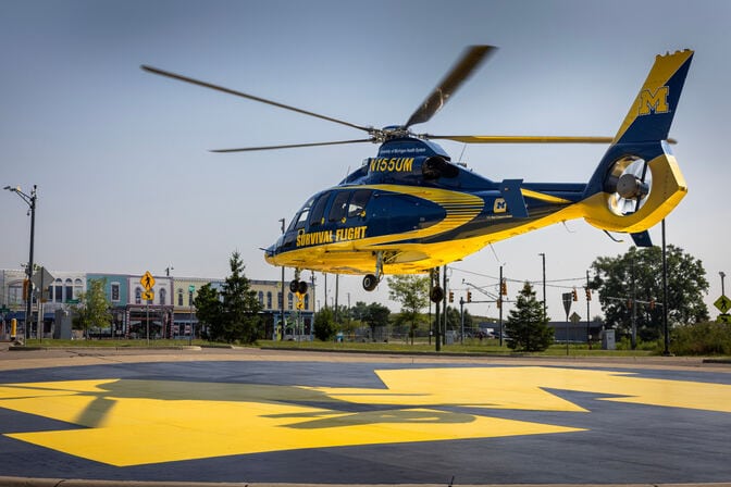 A helicopter painted in blue and yellow, with "SURVIVAL FLIGHT" written on the side, lands on a yellow block M.