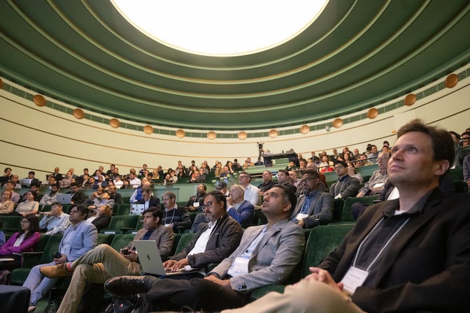 People mostly fill the amphitheatre, which has a capacity of 227. Near the front are speakers Markus Buehler (MIT), Surya Ganguly (Stanford), Lav Varshney (UIUC), and Venkat Viswanathan (U-M).