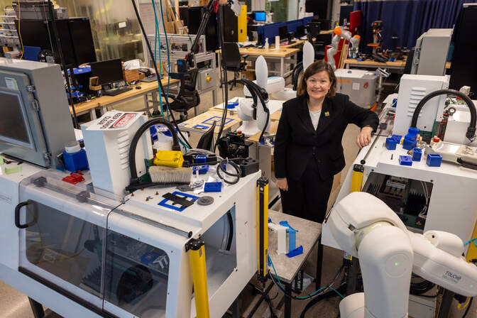 Tilbury stands in a large room among several boxy machines and robotic arms.