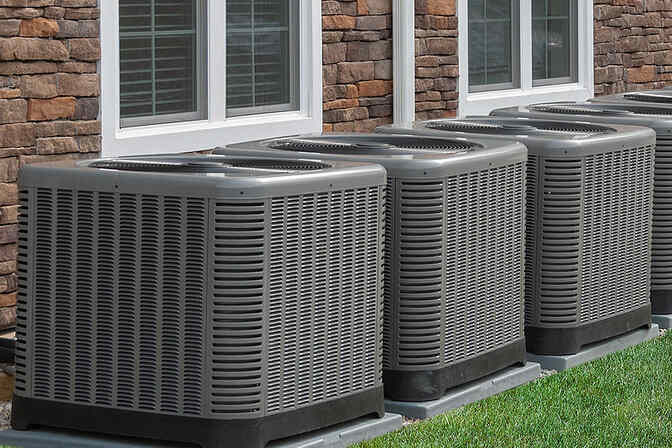 A line of AC units against a brick home.
