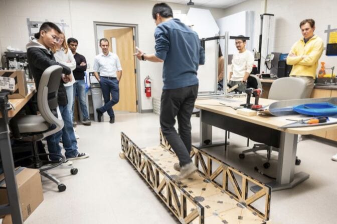 A person walks on a makeshift bridge structure in a lab while others watch.