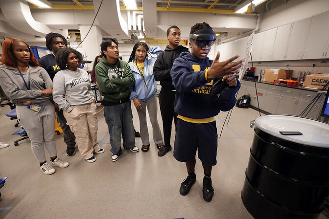 A group of young people in a lab, watching one person using a VR headset.