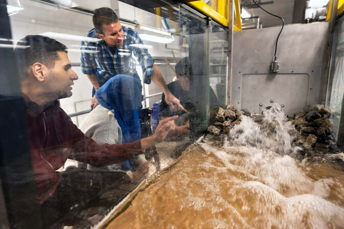 Four individuals examining water flow over rocks in a lab tank.