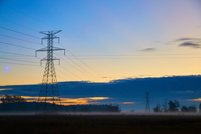 Power transmission towers and lines against a colorful sunrise or sunset sky.