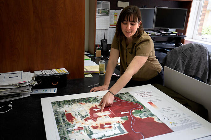 A women  leans over the map showing areas of the city of Goshen, IN that are prone to flooding.