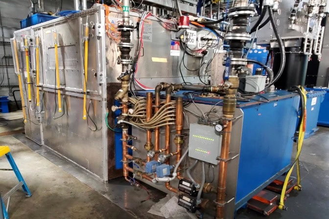 Industrial equipment featuring metallic structures, yellow hoses, copper pipes, blue box, and control panel with cables.