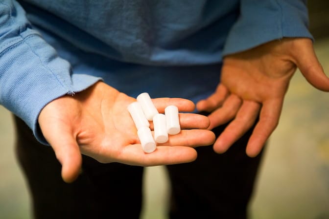 In his open palm, a man holds five white cylinders about an inch long and a quarter-inch wide.