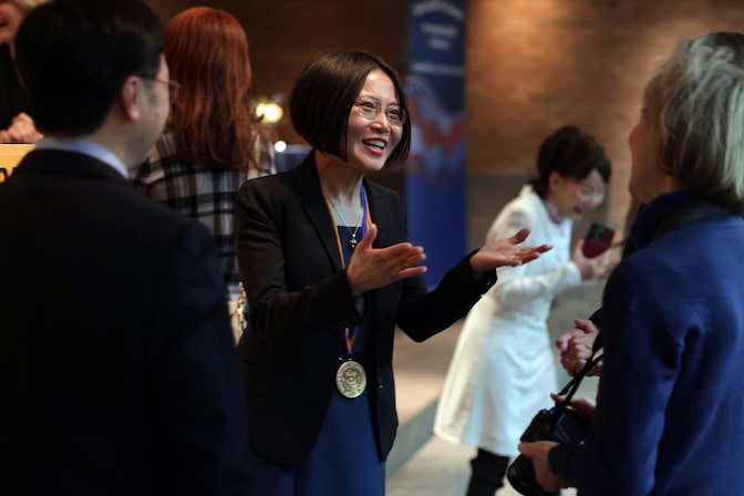 A woman with a medal around her neck engages in conversation at a social gathering.