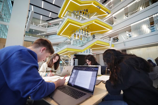 Students studying in a modern building with a multi-level yellow staircase and glass railings.