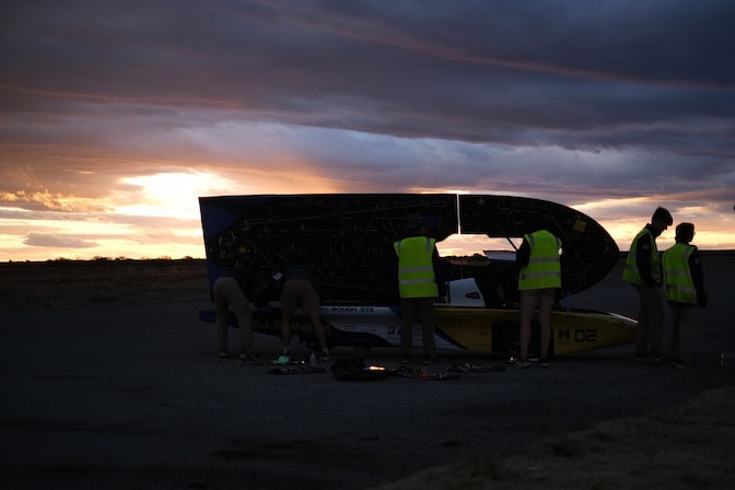 
The black silhouettes of the car's open hood, which resembles the profile of a bullet, and the race crew members add interest to an otherwise flat, twilight skyline. 