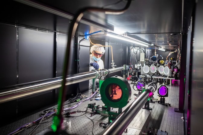 A laboratory with optical and ZEUS laser equipment, featuring a person in goggles adjusting the setup.