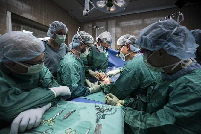 Surgeons and medical staff perform a procedure on a patient in an operating room with surgical tools on a table in the foreground.