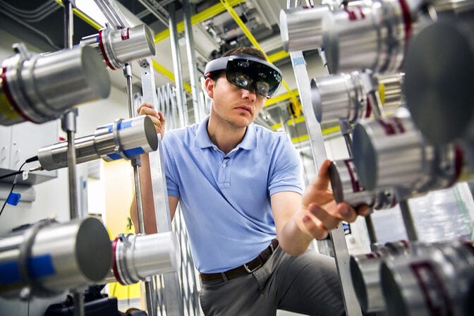 Person wearing augmented reality goggles inspecting metal components in an industrial setting.