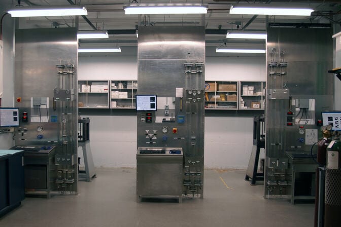Interior of a laboratory with metallic workstations, monitors, and gas cylinders.