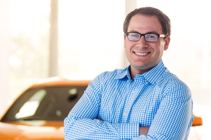 Portrait of Ira Goldberg in front of an orange Mustang.