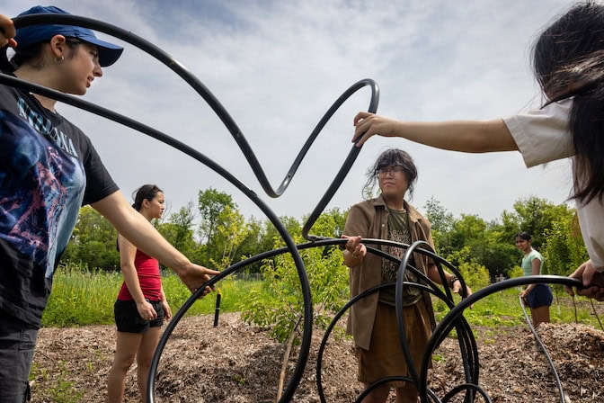 hree students straighten black tubing from a tangled coil. Behind them, two more students handle the tubing near rows of small trees.