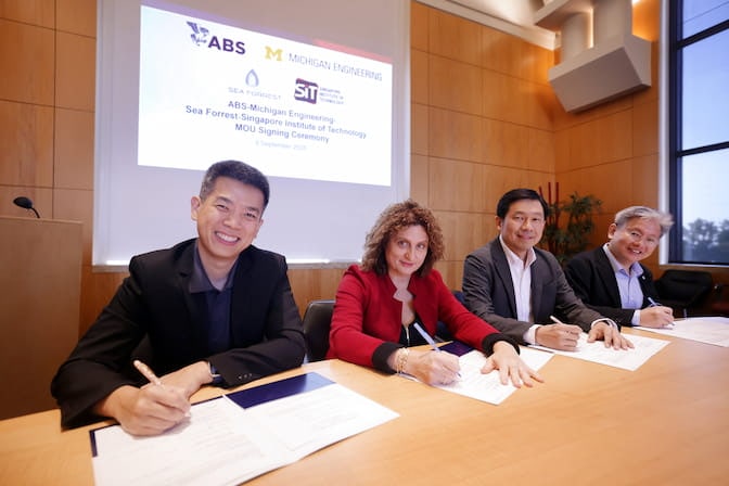 Four people sign a contract while sitting at a long desk. A screen behind them reads "MOU signing ceremony" and displays the logos and names of the University of Michigan, Sea Forrest, the American Bureau of Shipping, and Singapore Institute of Technology.