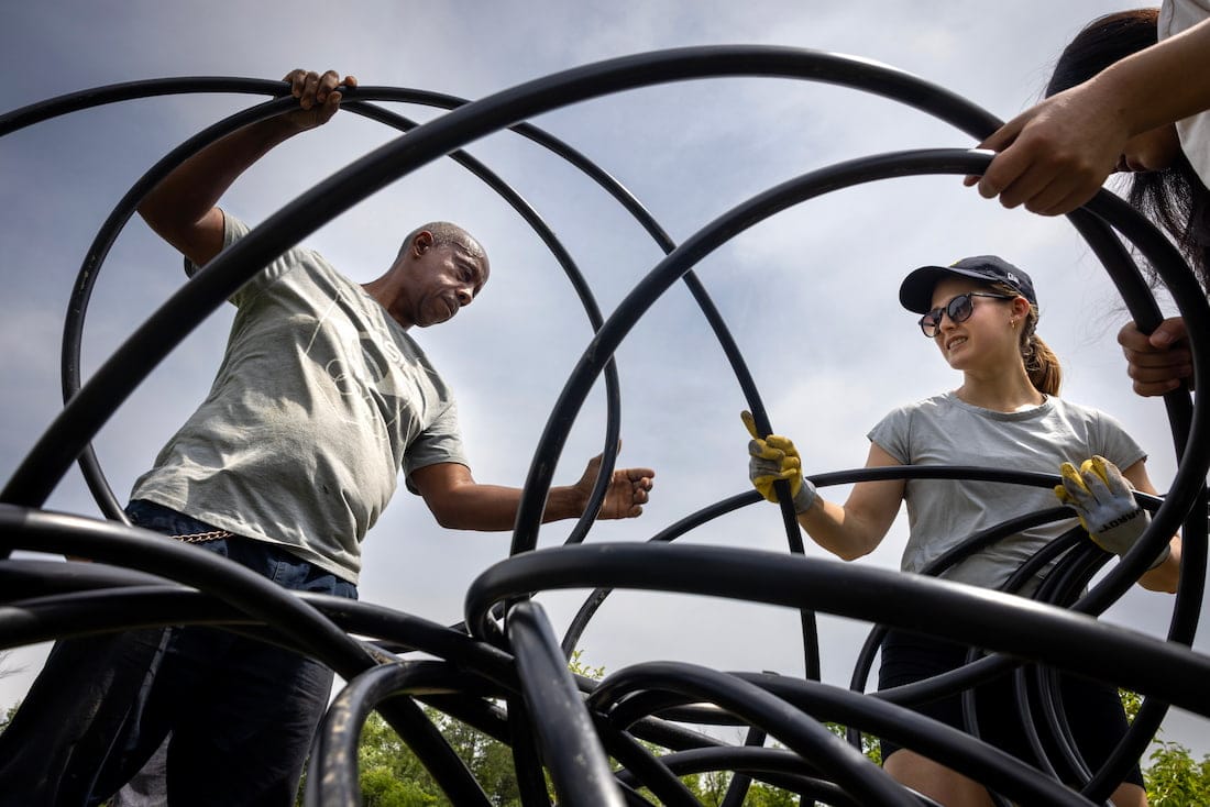 A man and a young woman hold a long, tangled piece of black tubing.