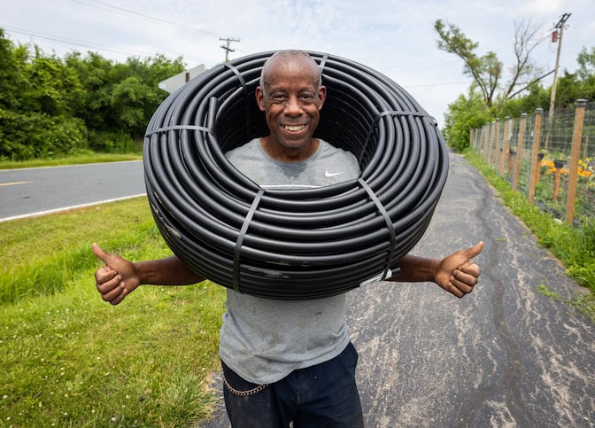  A man holds two thumbs up while wearing a large coil of black tubing around his neck. He is smiling.