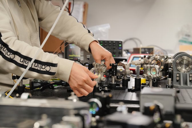 Person adjusting optical components on a laboratory table with scientific equipment.