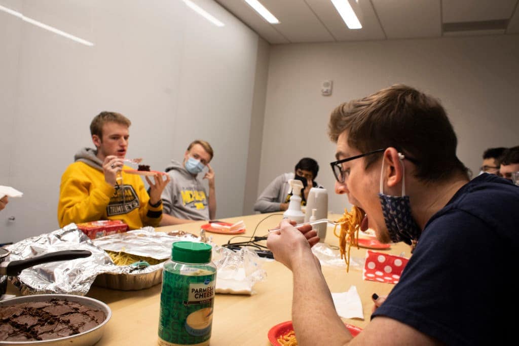Students eating spaghetti and brownies at a conference room table