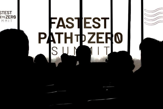 Silhouettes of an audience seated in front of windows displaying the text "FASTEST PATH TO ZERO SUMMIT."