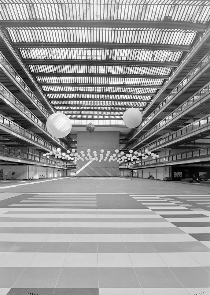 A black and white photo shows the cavernous atrium space inside an office building, with light streaming through its glass roof.