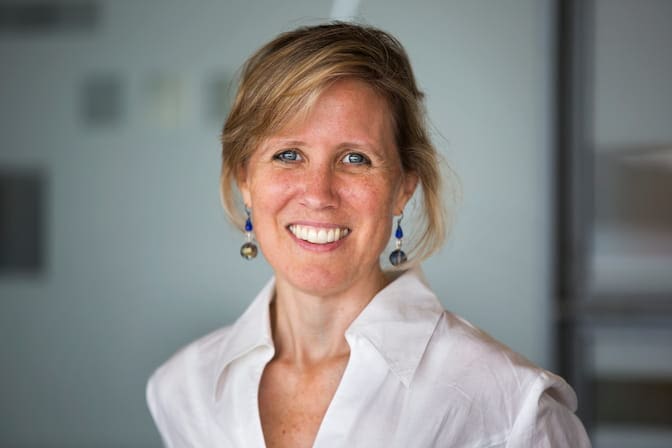 Portrait of a woman wearing a white oxford shirt and dangling earrings.
