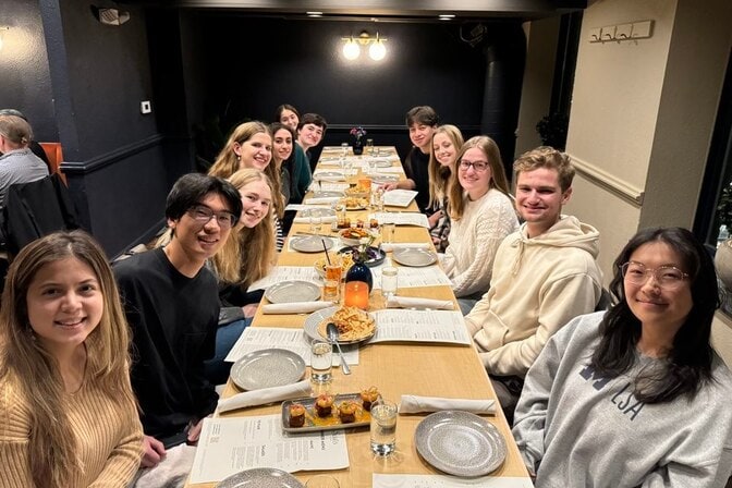 A group of thirteen people sitting around a long dining table with plates and appetizers in a dimly lit restaurant.