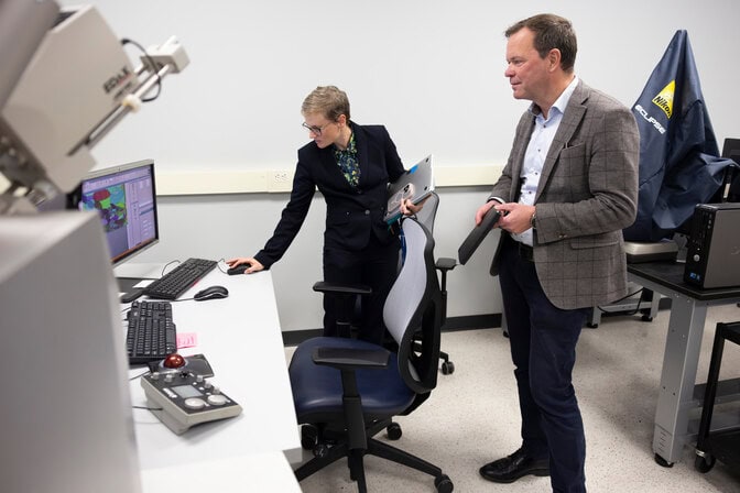 In a research lab, a woman stands in front of a computer and navigates while a man in a suit watches the demonstration. 