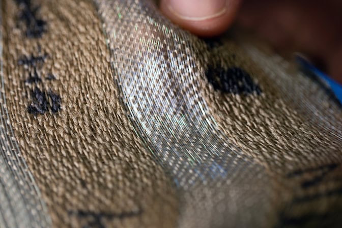 Close-up of shimmering photonic fibers in woven fabric with golden-brown hues and iridescent details.