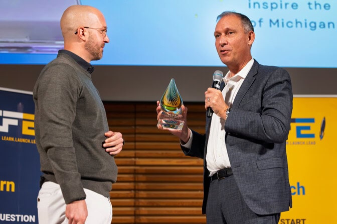 Thomas Zurbuchen presents an award to Jason Bornhorst on stage while announcing into a microphone.