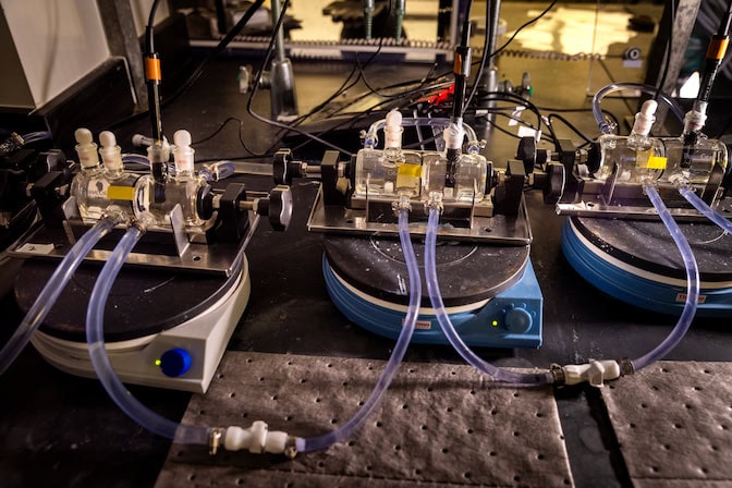 Three glass cylinders each hold water within two compartments that are separated by a membrane held by a black ring in the center of the cylinder. An external compartment around each cylinder is connected by plastic tubing. Each cylinder is placed on a platform on a lab bench.
