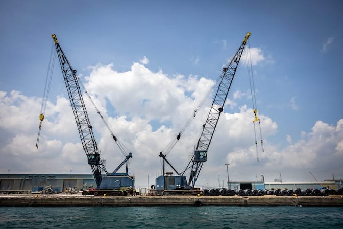 wo large cranes are stationed at a riverside terminal.