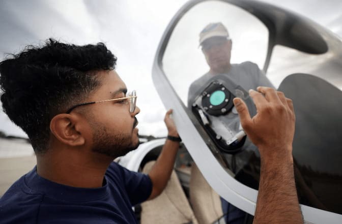Two men place a sensor inside the window of an airplane cockpit.