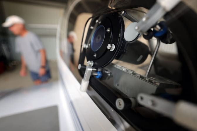 sensor, which resembles a black cylinder, is mounted inside the window of an airplane cockpit. A flat end of the sensor, which is covered by blue-tinted glass, is approximately level with the window and points out from the cockpit.