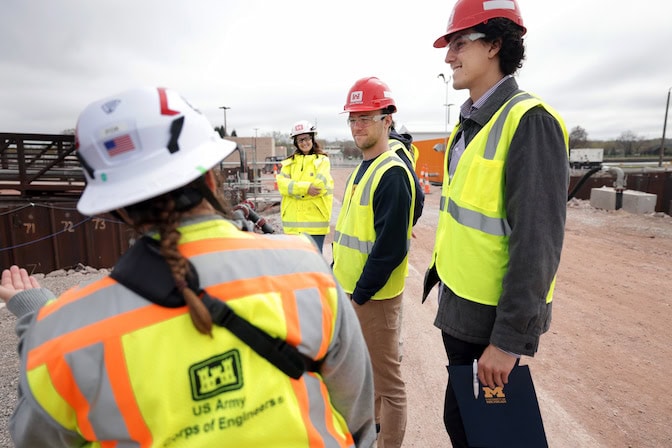 Two men and two women talk at a construction site. They are wearing hard hats and neon safety vests.