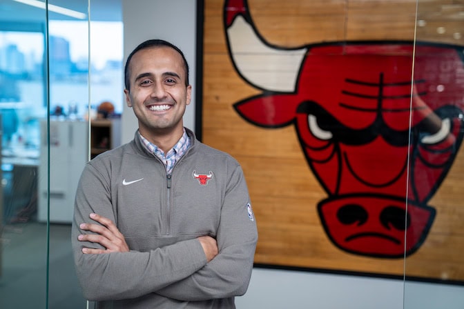 A portrait of Ujwal Bharath standing and smiling in an office setting with a Chicago Bulls logo in the background.