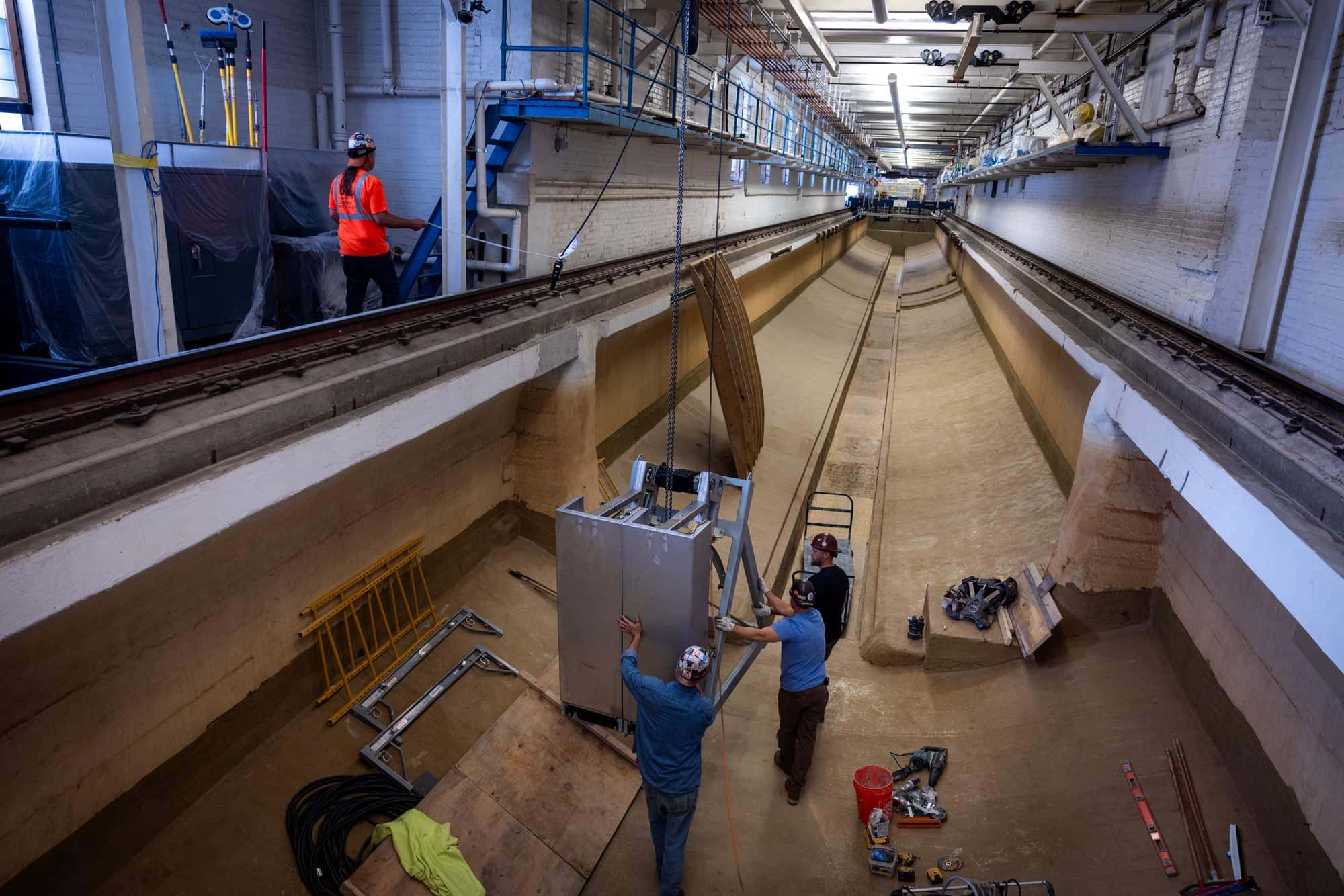 A team of contractors moves a new wave-maker machine part along the length of the MHL tow tank.