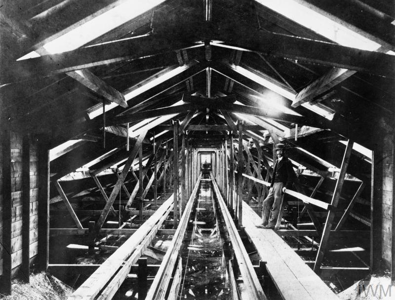 A man in a 19th century outfit stands inside of a wooden structure in a long tunnel.