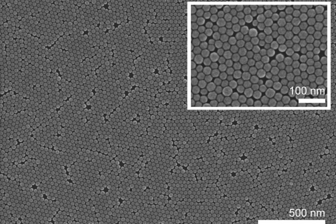 A gray-scale scanning electron microscope image of a nanocrystal layer taken from above. Tiny hexagons cluster together, touching but not overlapping. A cut-out in the far right zooms in 5 times, showing the hexagons in greater detail.