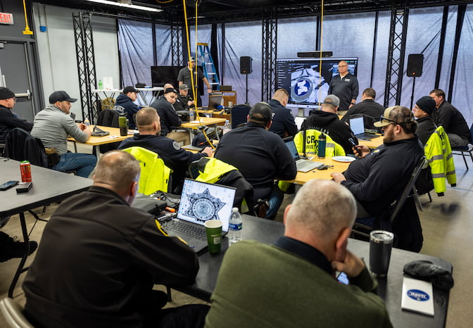 A group of people, some in a police uniform, seated at a desk, listen intently to a speaker.