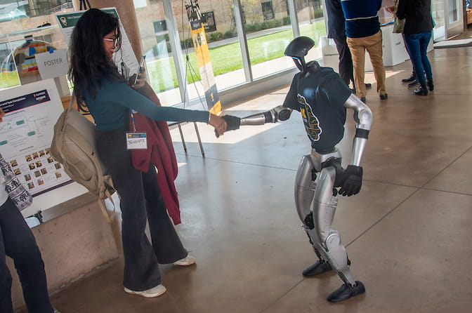 Person shaking hands with a humanoid robot in a hallway