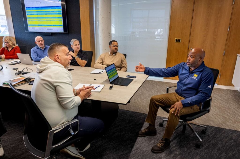 A group of people sits around a conference table listening to a man at the head of the table.