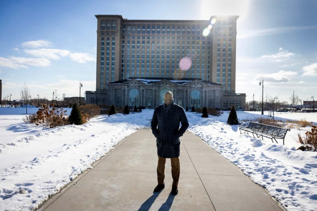 A smiling man stands in front of a building with snow on the ground.