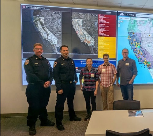 Four people stand in front of a screen displaying several maps of California.