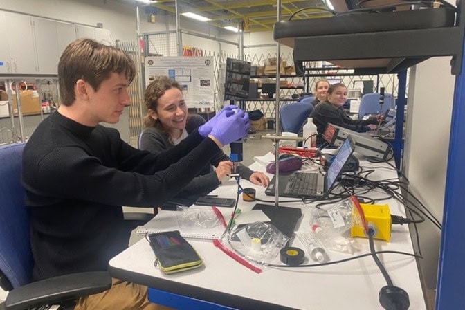  Four students sit and work at a long laboratory bench.