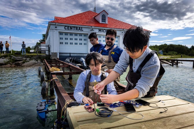 Four men gather around a dock. Two of them handle a set of wires connected to computer chips and a smart phone.