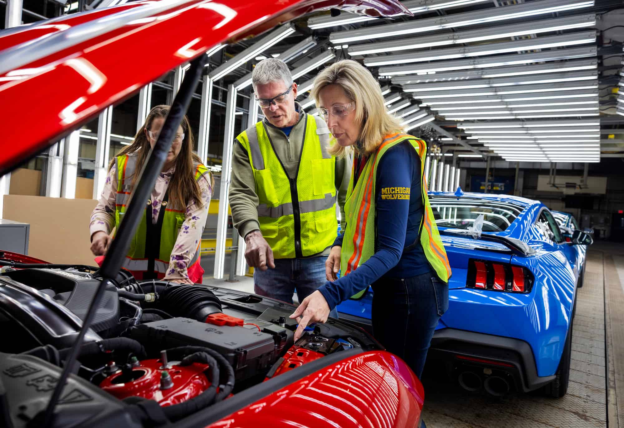 Engineers discuss details inside a Mustang’s engine bay while standing on the production line.